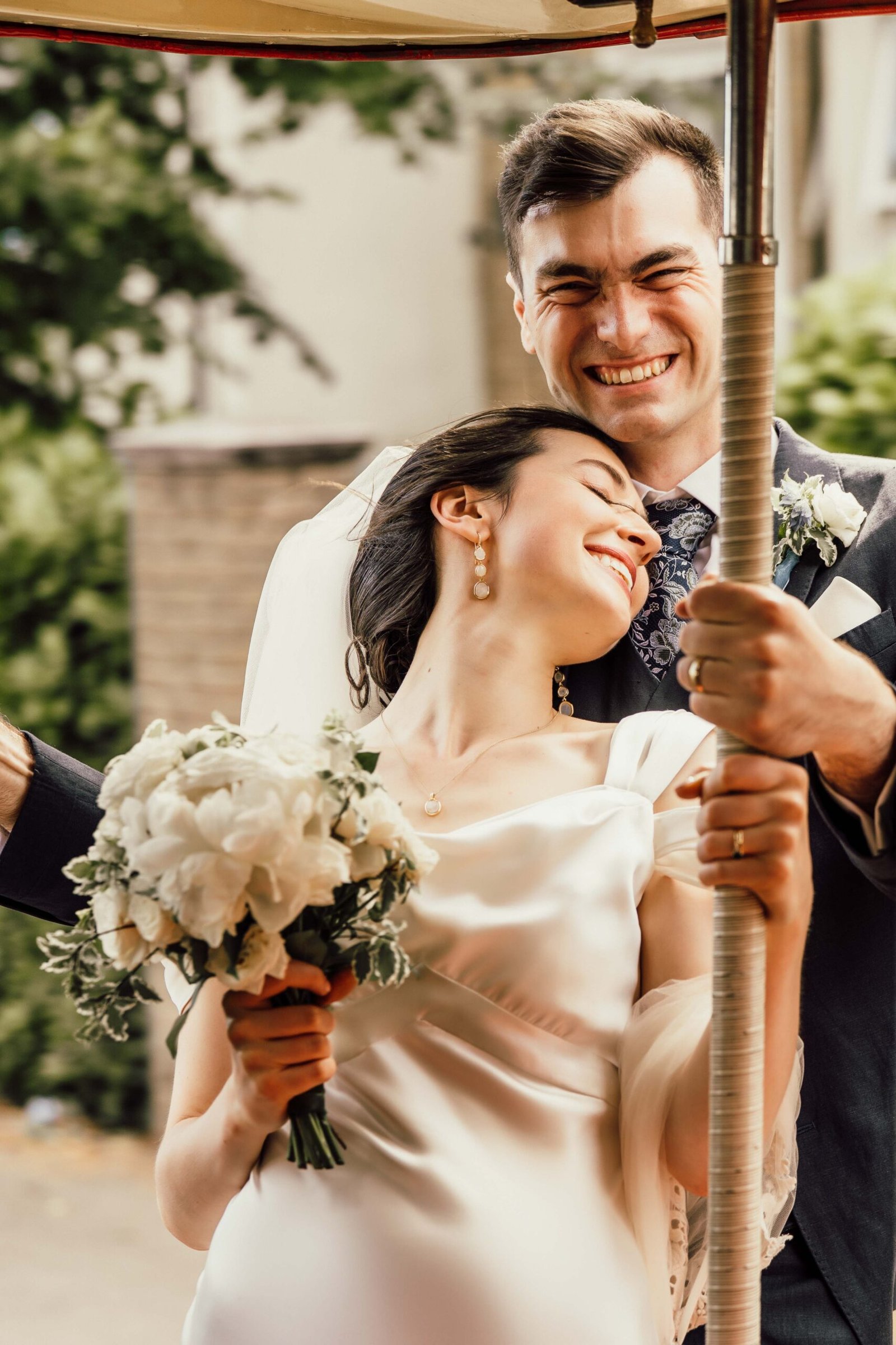 Bride leaning against her smiling groom while holding a white wedding bouquet
